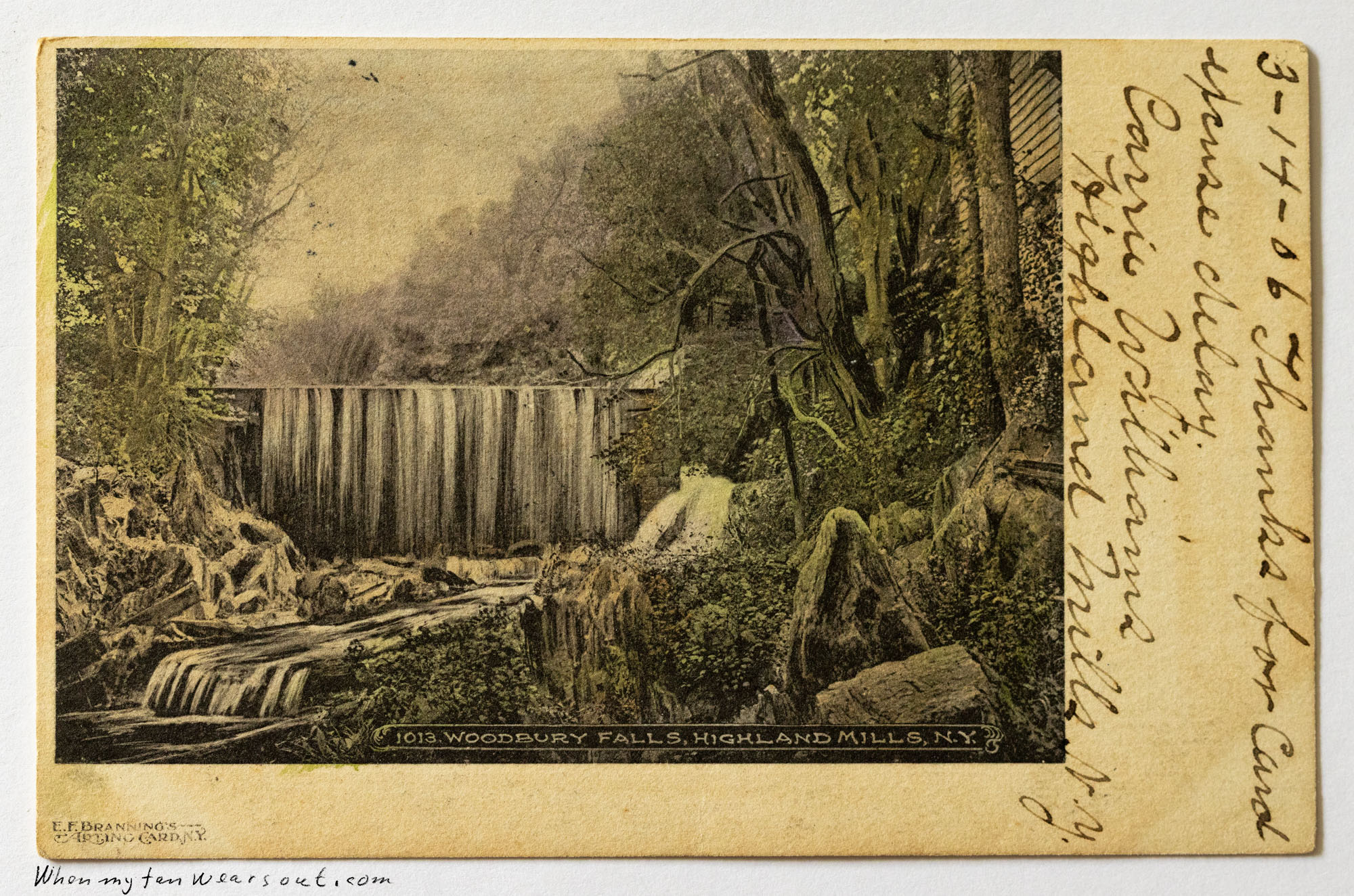 A hand-tinted postcard image of Woodbury Falls, Highland Mills, New York, showing a wide waterfall cascading over rocks into a stream below, surrounded by lush green trees and foliage. A handwritten message is visible on the right border with the date 3-14-06 and signed by Carrie.