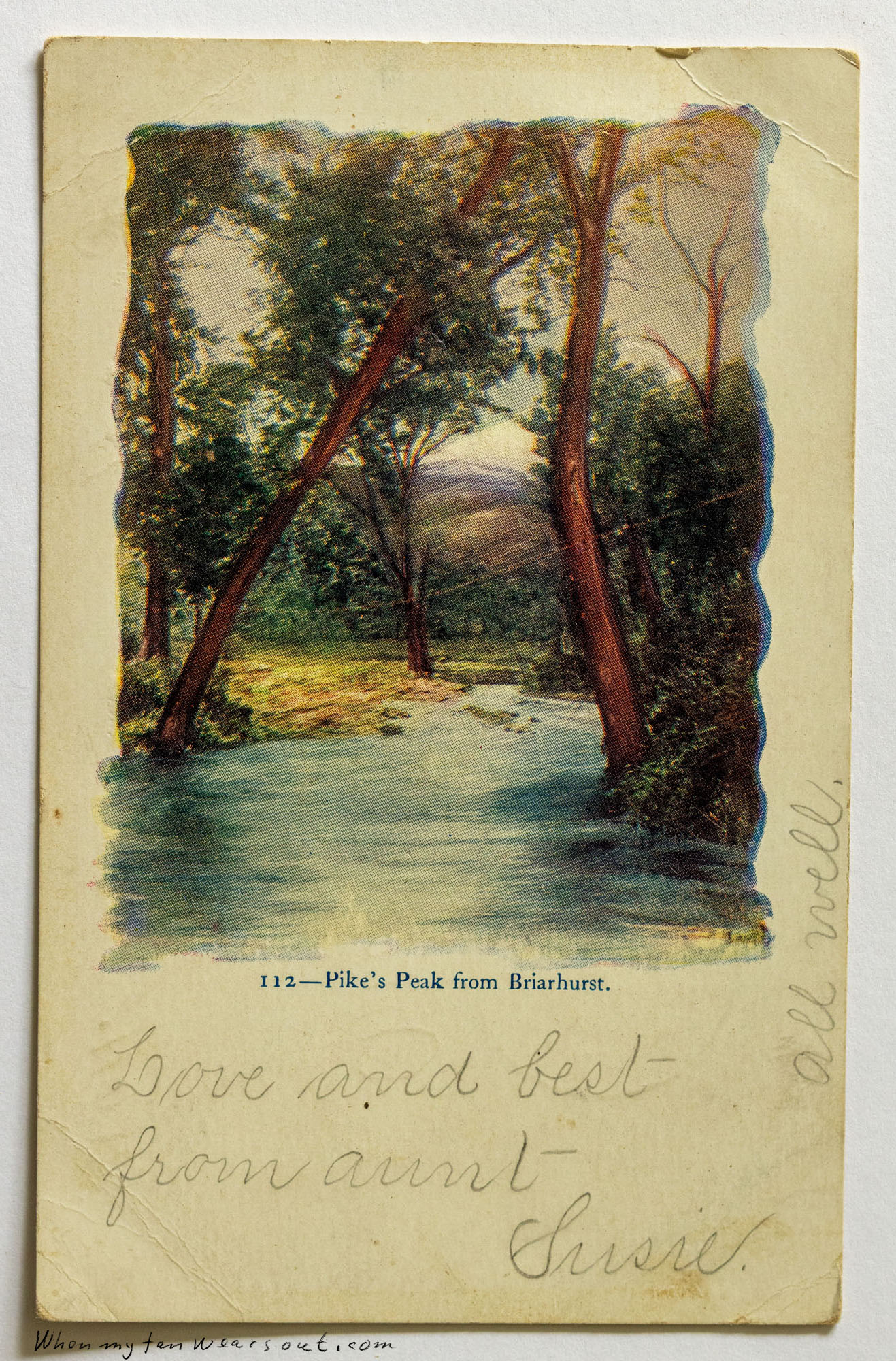 Front of postcard #0080: Colored landscape illustration depicting a stream flowing between trees, with a mountain peak (Pike's Peak) visible in t