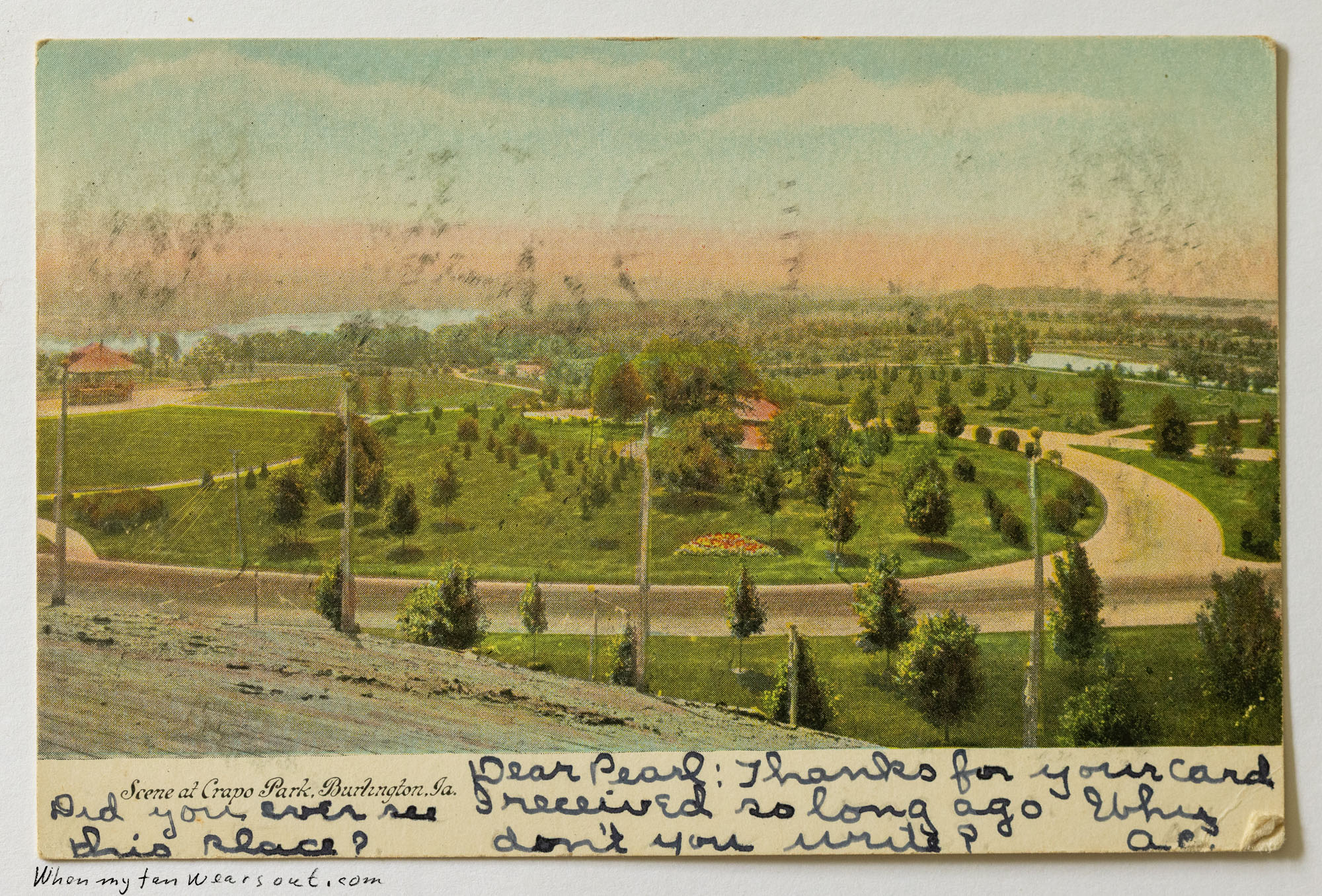 Front of postcard #0084: Illustrated postcard showing an elevated, wide scenic view of Crapo Park in Burlington, Iowa. Features lush green lawns,