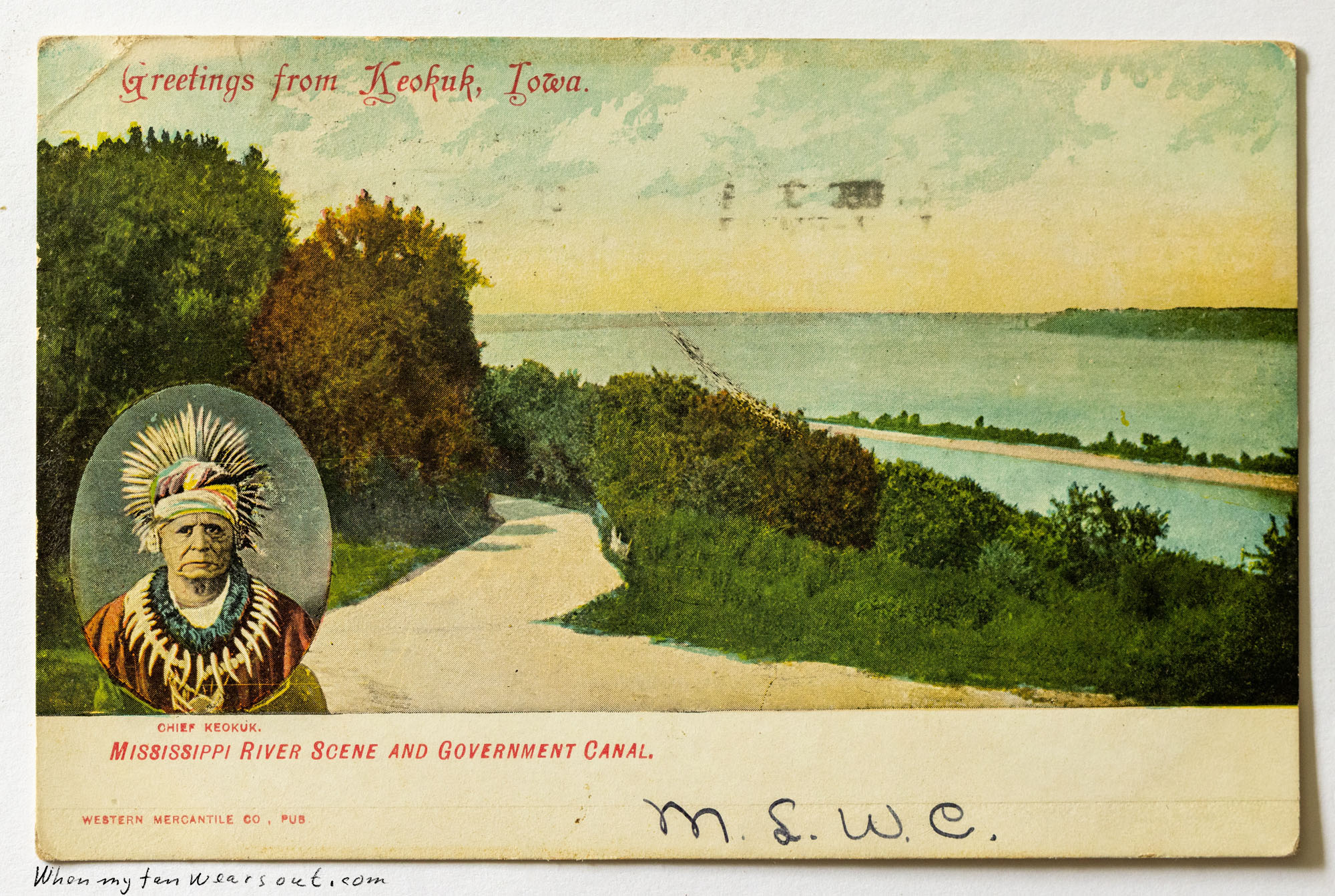 Front of postcard #0089: Colored postcard depicting a road sweeping past trees toward the Mississippi River and Government Canal under a soft yel