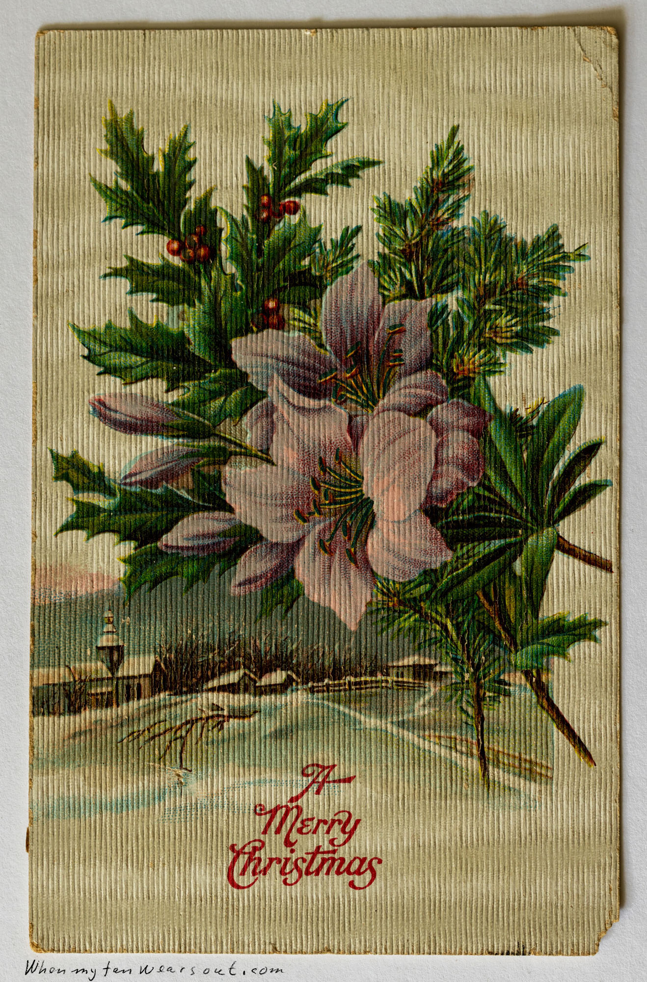 A vintage Merry Christmas postcard featuring a vibrant central arrangement of pink lilies with prominent green stamens, surrounded by dark green holly leaves with red berries, and deep green pine needles. In the soft, blurred background, a winter landscape with a bare tree and distant snow-covered buildings is visible. The words