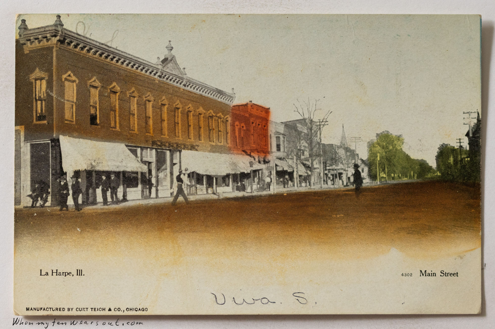 A vintage postcard depicting a lively Main Street in La Harpe, Illinois, circa early 1900s. The street is lined with multi-story brick buildings, some featuring striped awnings over ground-level shops. People are visible walking on the sidewalks and in the street. A prominent three-story brick building, partially hand-colored in red, stands further down the street. The sky is light, and trees are visible in the distance. The bottom left corner reads