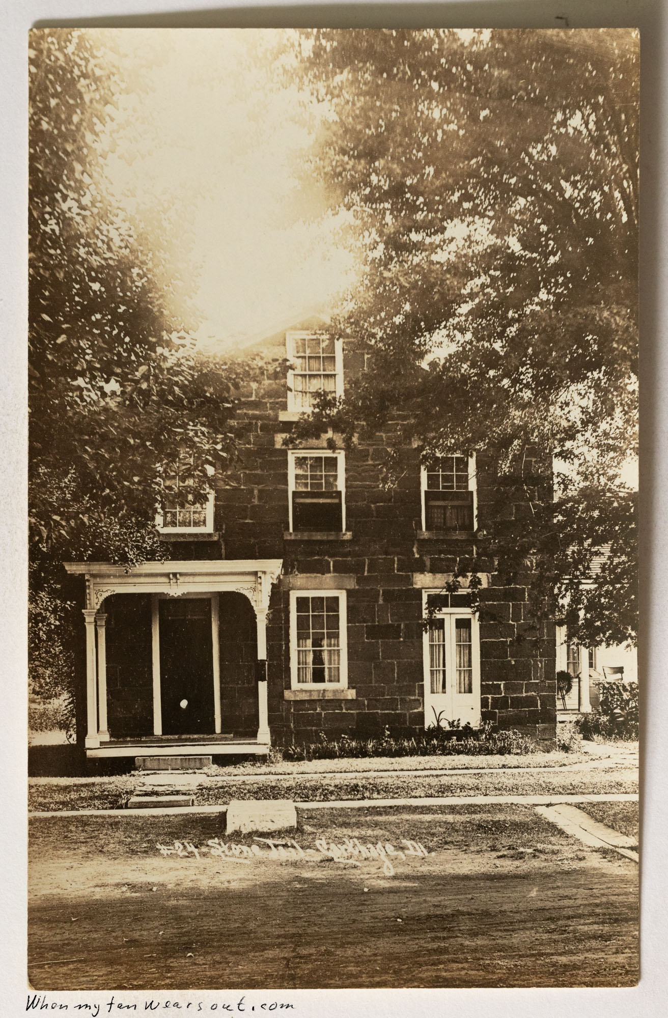 Front of postcard #1087: Real photo postcard (sepia tone) showing the "Stone Inn" in Carthage, Illinois. It is a two-story dark stone building wi